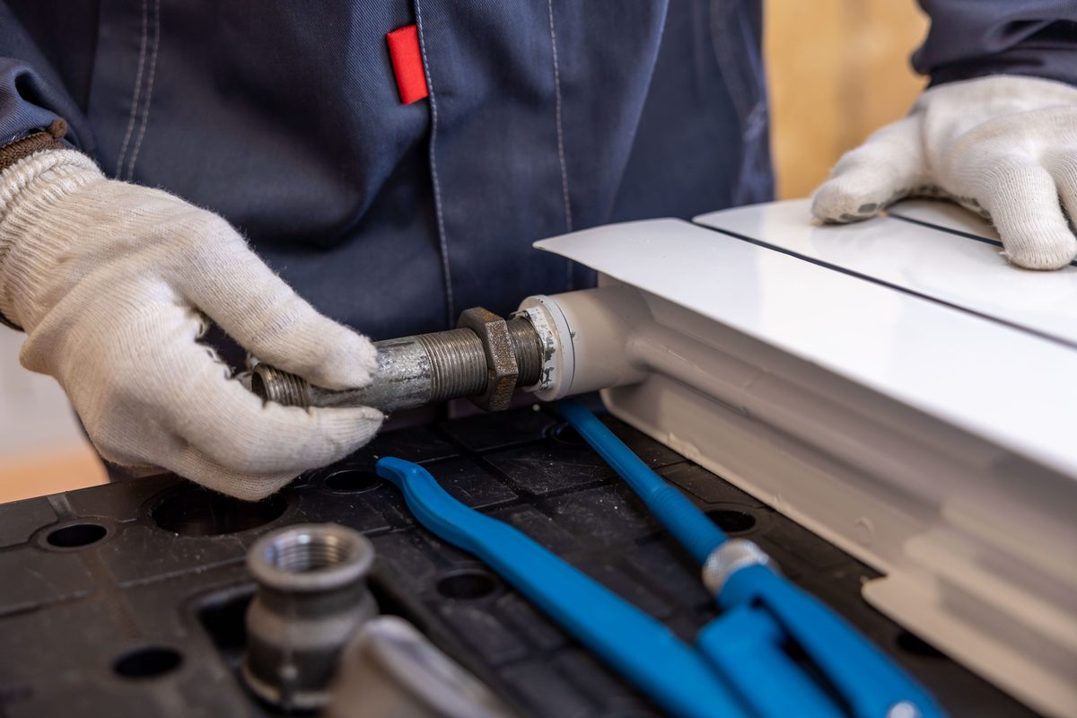 Installateur verpresst Rohrleitungen an einem Heizkörper
